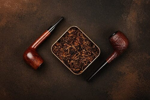 metal tin can of pipe tobacco and 2 tobacco pipes laying beside it